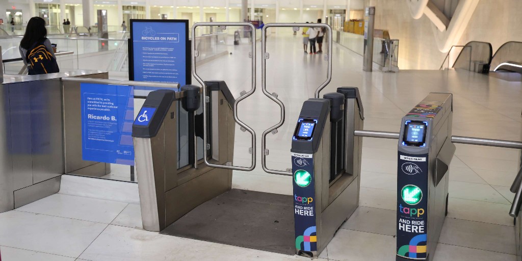 Wide ADA-accessible fare gate at a PATH station upgraded with TAPP contactless payment readers. The gate displays a green arrow indicator and 'TAPP and Ride Here' branding.